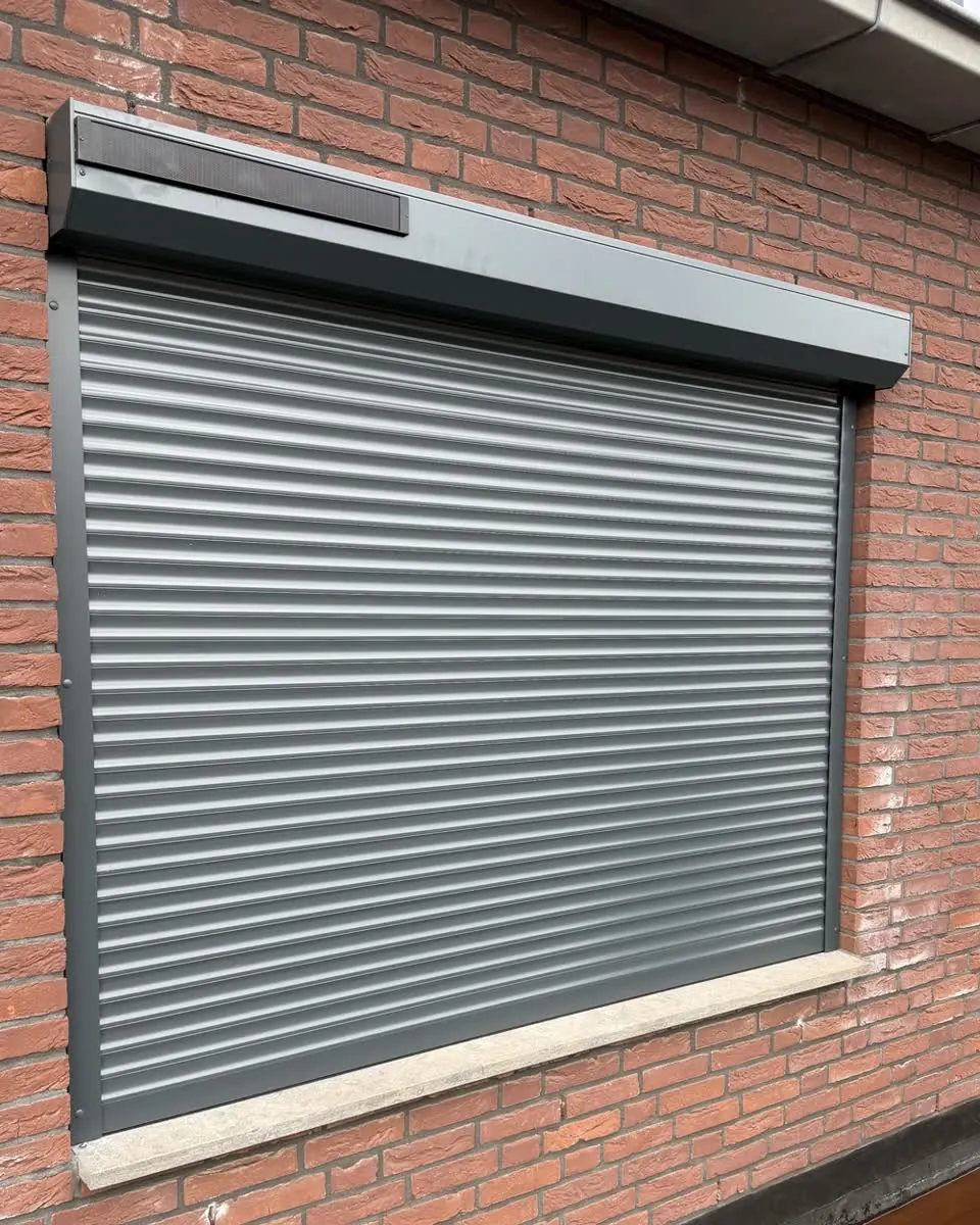 Gesloten antraciet solar rolluik aan de bakstenen achtergevel boven de aanbouw